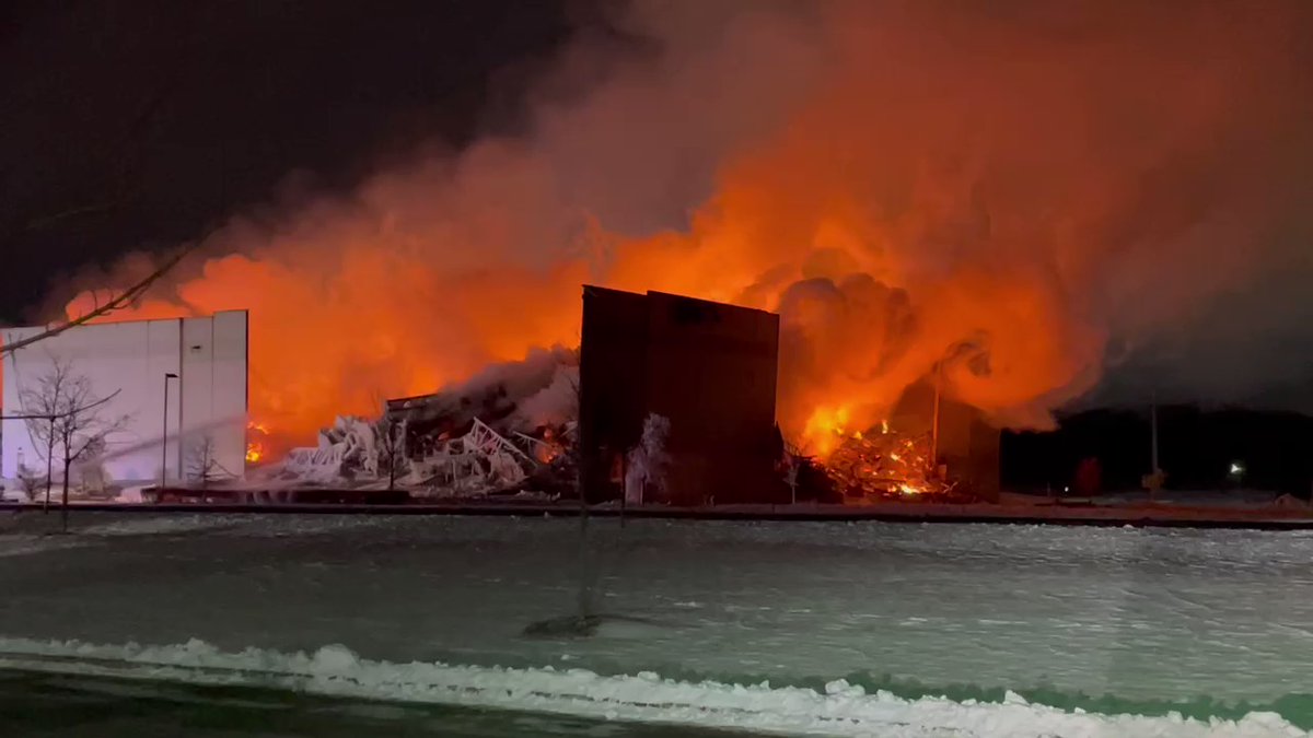 Smoke curls as firefighters shoot water at a burning warehouse in Bartlett, IL. Walls have collapsed. Company stores paper documents.